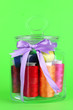 Glass jar containing various colored thread on green background