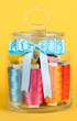 Glass jar containing various colored thread on yellow