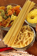 Different types of pasta, spices, tomatoes on a wooden table