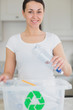 Smiling woman throwing bottle into recycling bin