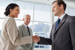 Smiling business people shaking hands with smiling colleague beh
