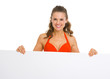 Smiling young woman in swimsuit showing blank billboard