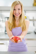 Smiling teenager girl giving apple in kitchen