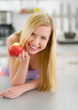 Happy teenager girl eating apple in kitchen