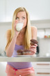 Teenager girl eating chocolate muffin with milk in kitchen