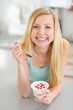 Smiling teenager girl eating yogurt in modern kitchen
