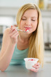 Happy teenager girl enjoying yogurt in kitchen
