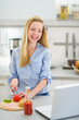 Happy girl making sandwich in kitchen and looking in laptop