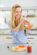 Happy young woman making sandwich in kitchen