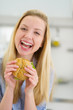 Smiling teenager girl eating sandwich in kitchen