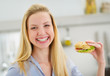 Happy teenager girl eating sandwich in kitchen