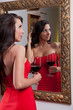 Sensual elegant young woman in red dress looking into mirror