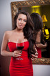 Sensual elegant young woman in red dress looking into mirror