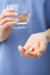 Doctor's hands holding two pills and a glass of water