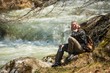 Young hiker woman sitting  near fast river 
