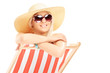 Young smiling female with a hat posing on a beach chair