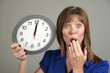Woman with surprised expression holding a clock