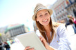 Cheerful girl with hat using tablet in town