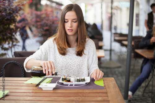Photo: Young woman pouring soy sauce on sushi plate Young woman pouring soy sauce on sushi plate