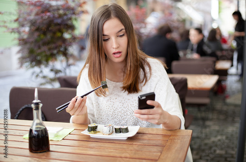 Photo: Young woman texting while eating sushi in a restaurant Young woman texting while eating sushi in a restaurant