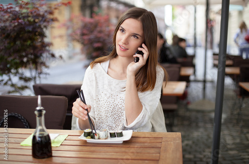 Photo: Beautiful young woman talking on the phone in a sushi restaurant Beautiful young woman talking on the phone in a sushi restaurant