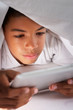 Boy Using Digital Tablet Under Duvet