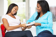 Two Women Sitting On Sofa Exchanging Gifts