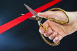 Hand cutting the red ribbon with scissors.