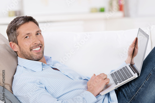 Photo: lächelnder mann liegt mit laptop auf dem sofa lächelnder mann liegt mit laptop auf dem sofa