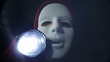 Scary masked man with torch in darkness
