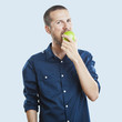 Cheerful beautiful man eating apple, isolated over white backgro