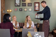 Waiter With Tray Of Glasses While Female Customers Having Meal