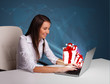 Pretty lady sitting at desk and typing on laptop with present bo