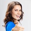 Foto: Young woman with thumbs up gesture, over grey Young woman with thumbs up gesture, over grey