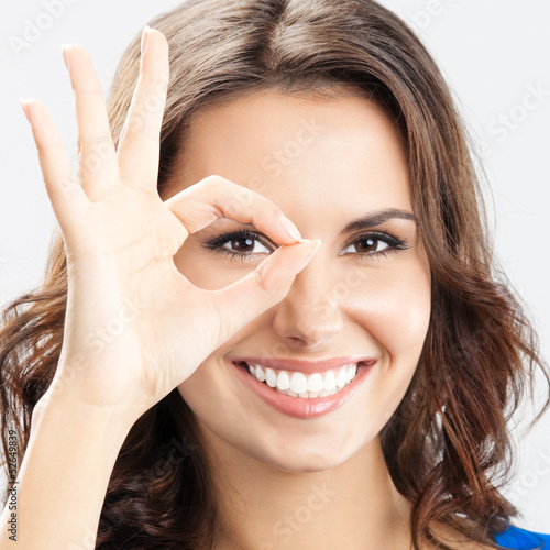 Photo: Young woman showing okay gesture, over grey Young woman showing okay gesture, over grey
