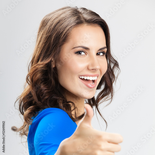 Photo: Young woman with thumbs up gesture, over grey Young woman with thumbs up gesture, over grey