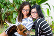 Two Asian girlfriends reading magazine