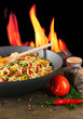 Noodles with vegetables on wok on fire background