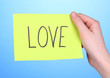 Photo: Love word on piece paper in hand on blue background Love word on piece paper in hand on blue background