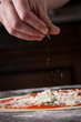 Cook putting oregano on raw pizza close-up