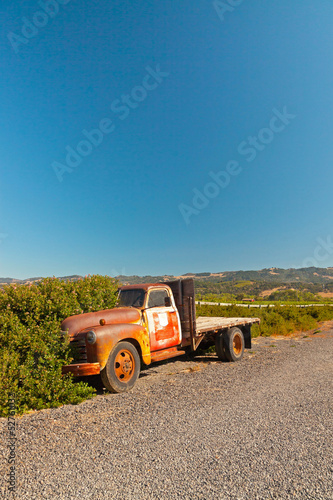 Photo: Old rusty pickup truck standing in winery landscape with blue sk Old rusty pickup truck standing in winery landscape with blue sk