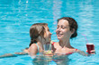 Mother and daughter swimming in pool with drink in hand