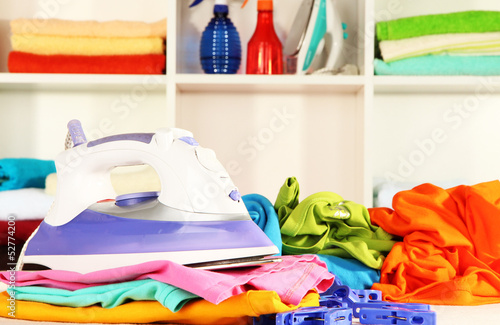 Photo: Clothes and iron on table on shelves background Clothes and iron on table on shelves background