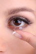 Young woman putting contact lens in her eye close up