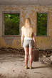 Young woman standing with vintage suitcase in abandoned building