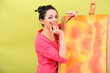 Beautiful young woman painter at work, on color background