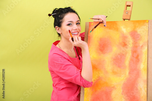 Photo: Beautiful young woman painter at work, on color background Beautiful young woman painter at work, on color background