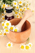 Essential oil and chamomile flowers in mortar on wooden table