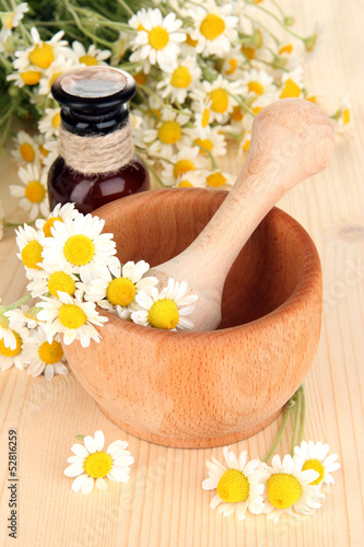 Photo: Essential oil and chamomile flowers in mortar on wooden table Essential oil and chamomile flowers in mortar on wooden table