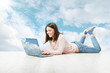 Photo: woman typing on laptop notebook, lying over sky background woman typing on laptop notebook, lying over sky background